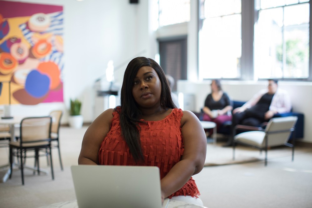 A Black women in a red shirt using a laptop and contemplating.
