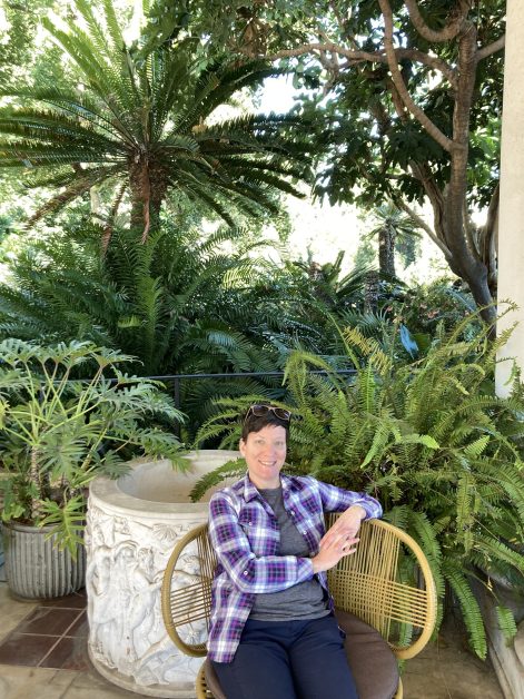 Lindsey in a purple plaid shirt, sitting in a garden of ferns.